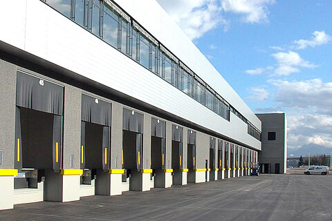 Referenzbild der Plattenhardt+Wirth GmbH mit fertigem Industriebau/gewerbebau. Merkmal ist die Front mit etlichen Anfahrrampen und darüberliegendem Büroanteil für Logistische Zwecke.